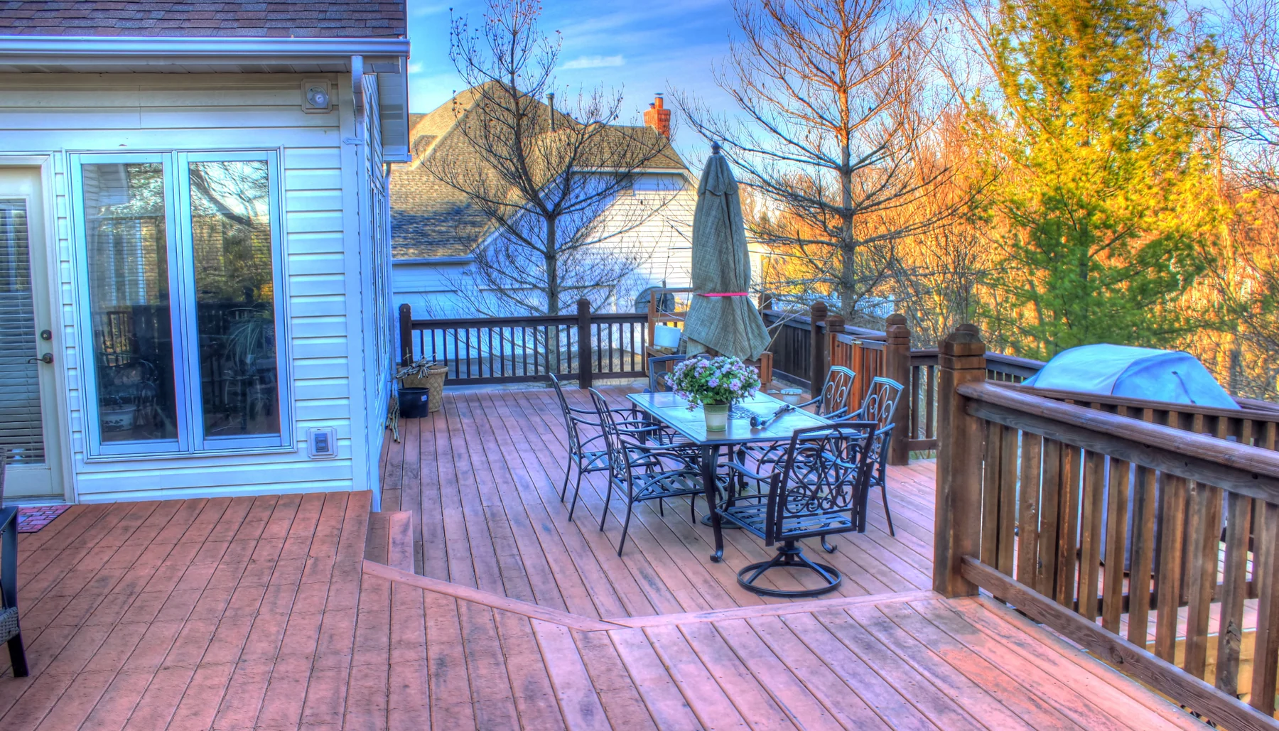 Deck with patio furniture and a table umbrella beside autumn trees